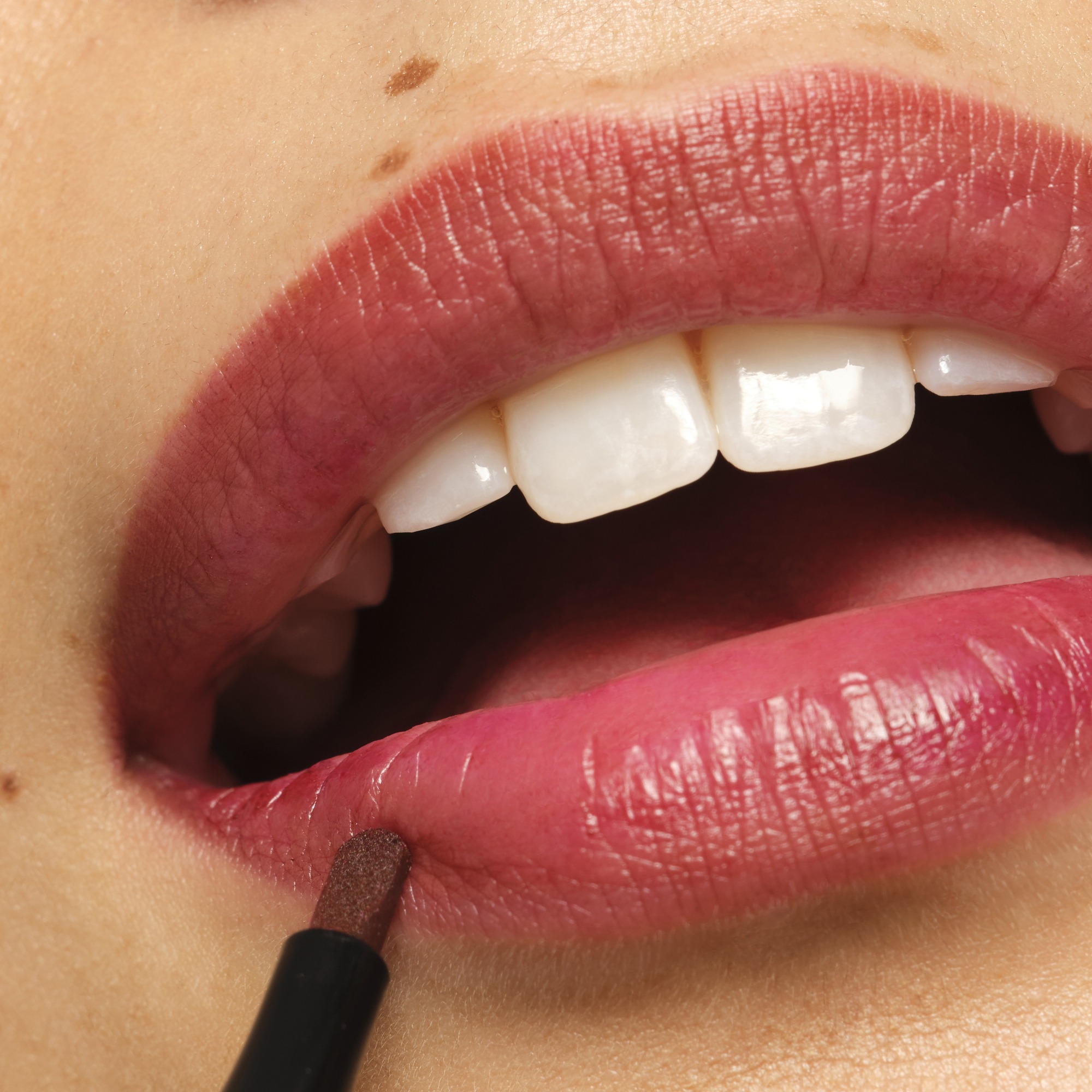 Close-up of a person’s lips, slightly parted, with a small mole above the upper lip and a black applicator near the lower lip.